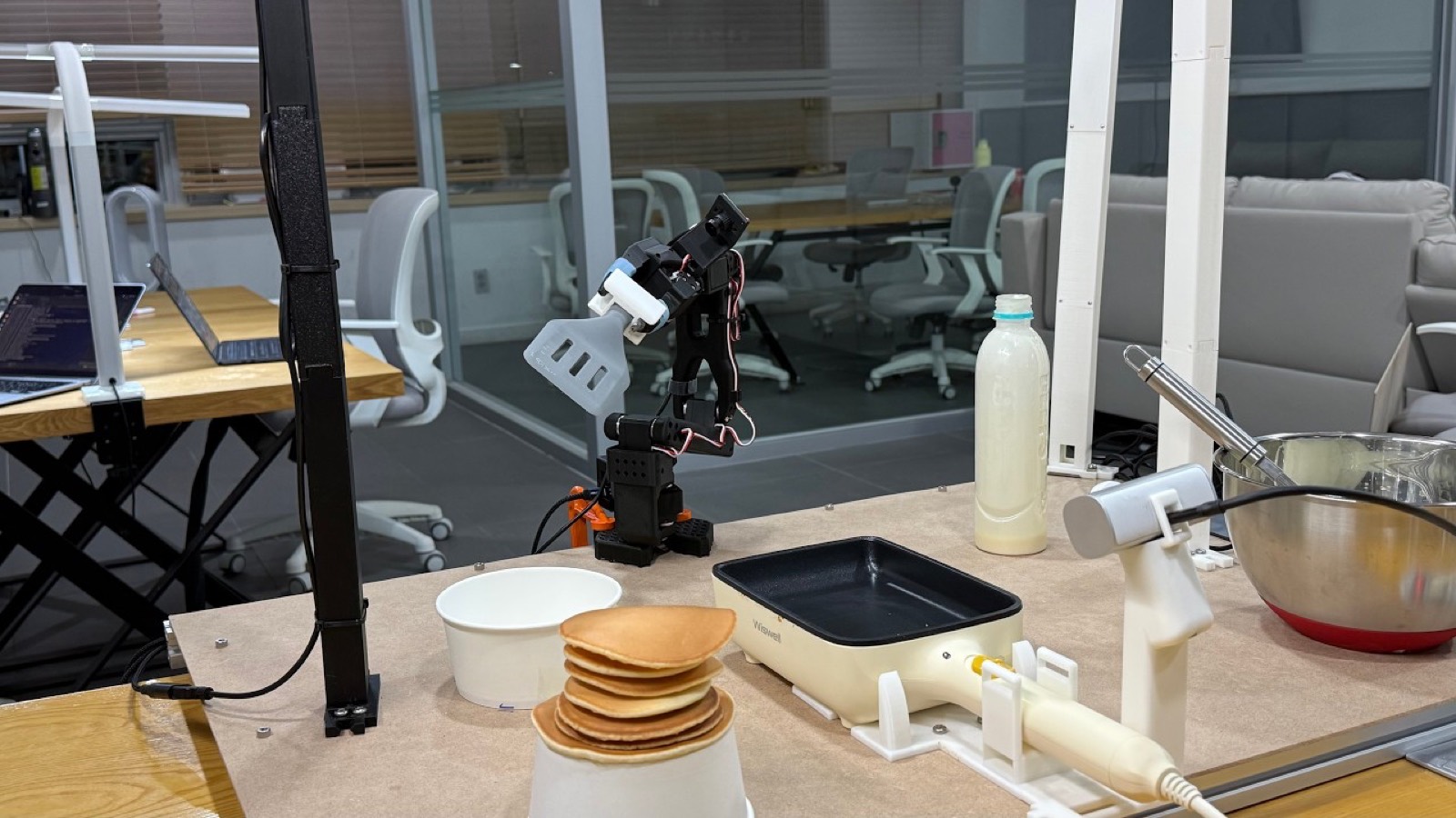 The Panbot workstation with the SO-ARM101 arm, griddle, batter dispenser, and finished pancakes